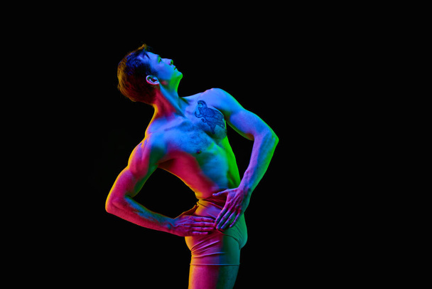 Dreaming dancer. Portrait of one young attractive man, actor with naked torm posing over dark studio background with neon light. Weightless, flexible. Grace, art, beauty, contemporary dance concept - Φωτογραφία, εικόνα