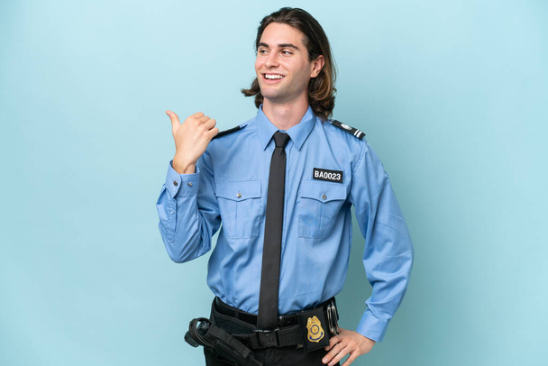 Молодой кавказский полицейский, изолированный на синем фоне, указывает на сторону, чтобы представить продукт - Фото, изображение