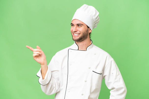 Νεαρός όμορφος σεφ πάνω από απομονωμένο φόντο δείχνοντας το δάχτυλο στο πλάι και παρουσιάζοντας ένα προϊόν - Φωτογραφία, εικόνα