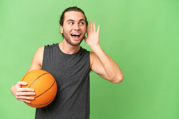 Jeune joueur de basket-ball homme sur fond isolé écouter quelque chose en mettant la main sur l'oreille - Photo, image