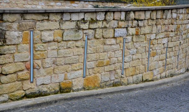 beautifully folded retaining wall with granite attic with small joints. brown beige yellow irregular gneiss holding slope above it. long vertically placed lights inside the wall. entrance to garage - Φωτογραφία, εικόνα