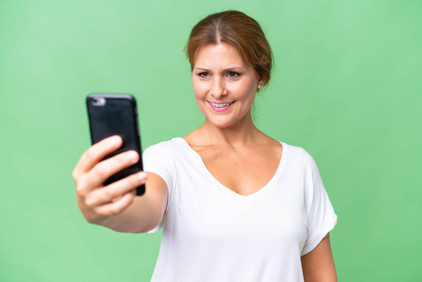 Mulher caucasiana de meia idade sobre fundo isolado fazendo uma selfie com telefone celular - Foto, Imagem