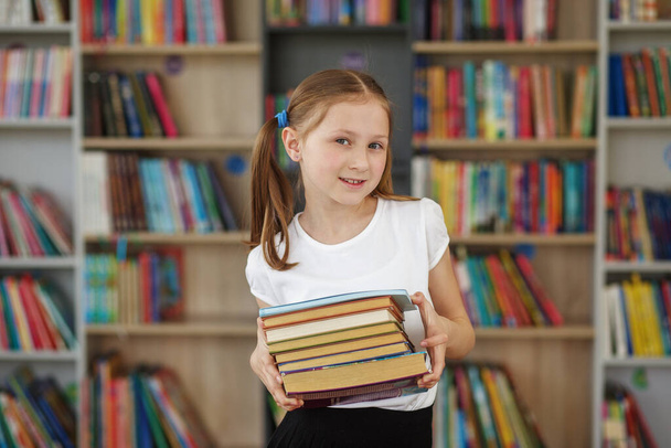 El niño compra libros en la librería para aprender o leer. Chica eligiendo un libro en la biblioteca escolar. Beneficios de la lectura cotidiana. - Foto, imagen
