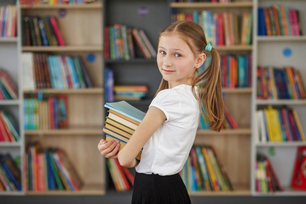 Çocuk öğrenmek ya da okumak için kitapçıdan kitaplar satın alır. Okul kütüphanesinde kitap seçen bir kız. Günlük okumanın faydaları. - Fotoğraf, Görsel