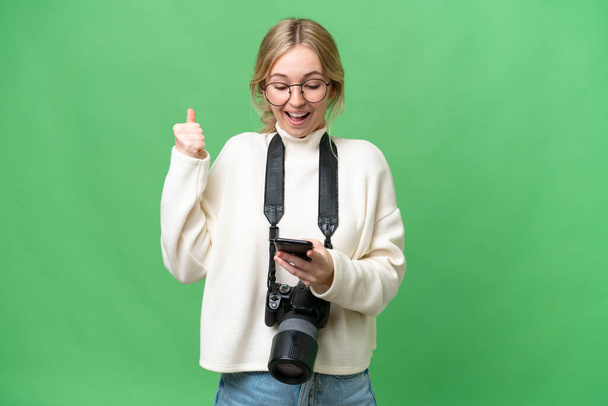 Mladý fotograf anglická žena přes izolované pozadí překvapen a posílání zprávy - Fotografie, Obrázek