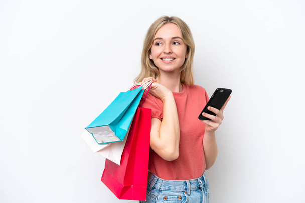 Young English woman isolated on white background holding shopping bags and a mobile phone - Foto, Imagem