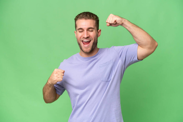 Young handsome caucasian man isolated on green chroma background celebrating a victory - Photo, Image