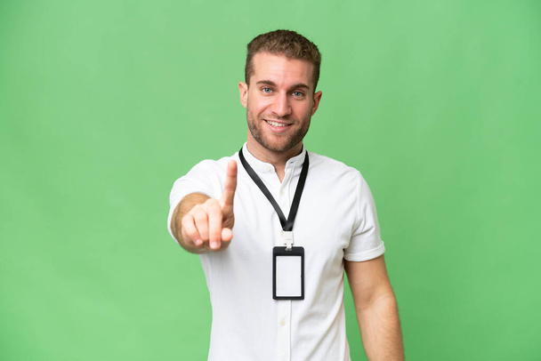 Young caucasian man with ID card isolated on green chroma background showing and lifting a finger - Photo, Image