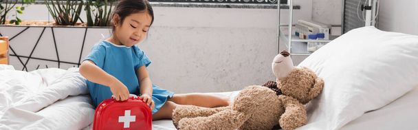 asiatique enfant ouverture jouet premiers soins enfant près ours en peluche sur lit d'hôpital, bannière - Photo, image