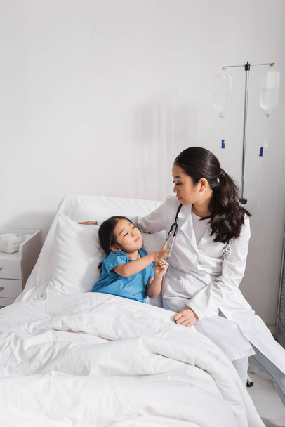 цікава азіатська дівчина торкається стетоскопа біля лікаря в лікарні
 - Фото, зображення
