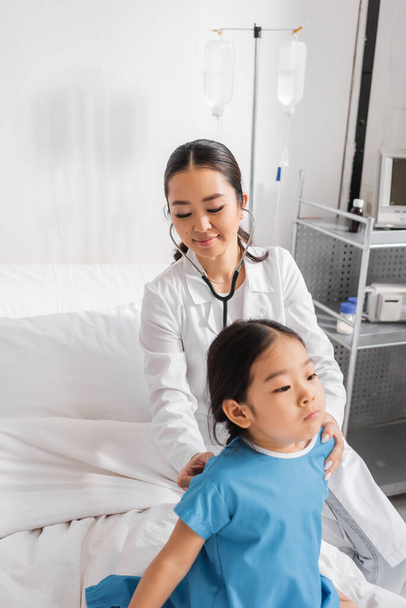 usmívající se asijský lékař se stetoskopem vyšetření malý pacient v nemocnici - Fotografie, Obrázek