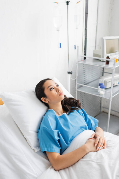 alto ángulo vista de enfermo y estresado asiático mujer acostado en hospital cama y mirando hacia otro lado - Foto, Imagen