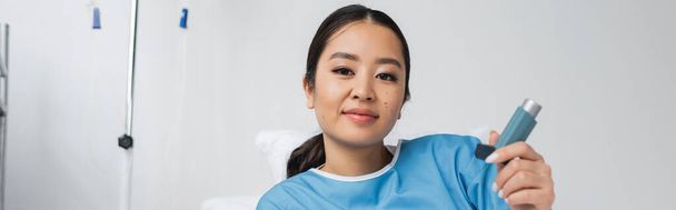 tyytyväinen aasialainen nainen pitelee inhalaattoria ja katselee kameraa klinikalla, banneri - Valokuva, kuva