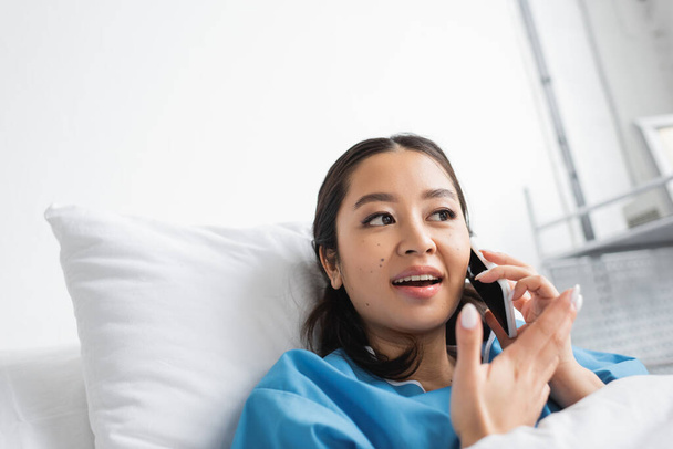 удивленная азиатка разговаривает по мобильному телефону и жестикулирует в больничном отделении - Фото, изображение