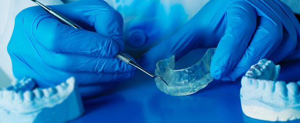 un dentista está ajustando una férula oclusal, utilizando una herramienta de metal, en un formato panorámico para usar como banner web o encabezado - Foto, Imagen