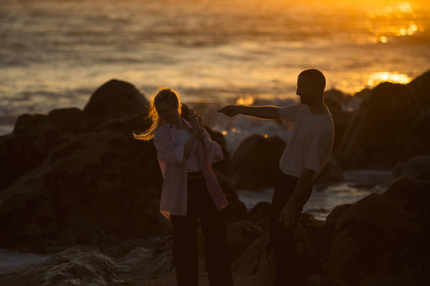A young couple in love fooling around on the rocky oceanfront during an amazing sunset.  - Фото, зображення