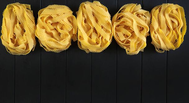 Italian pasta. Curly pappardelle pasta isolated on black background. Healthy food. Overhead view. Cooking concept. Copy space. - Photo, Image
