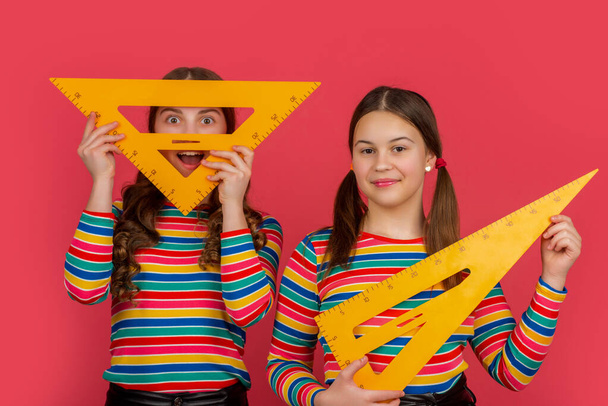 smiling school girls hold math tool of triangle. - Zdjęcie, obraz