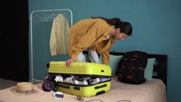 Valise de voyage de préparation à la maison. Femme essayant de fermer la valise avec beaucoup de choses sur le lit. Concept de voyage. Espace de copie - Séquence, vidéo