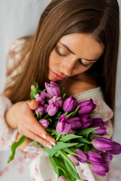 Portret seksownej młodej kobiety z długimi włosami. Model z bukietem liliowych tulipanów na białym. Wiosną. Wakacje. - Zdjęcie, obraz