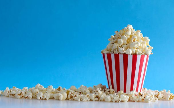 Tasty salted popcorn isolated on blue background. Cinema, movies and entertainment concept. Copy space. - Photo, Image