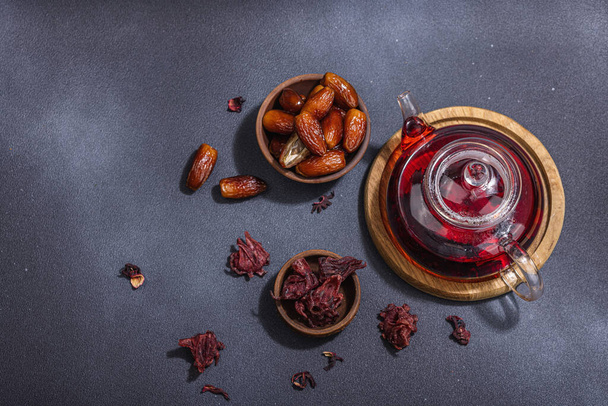 Hibiscus hot tea with dates. Traditional Ramadan Kareem concept snack for Iftar or Suhoor meal on dark stone concrete background. An arabian sweet treat, hard light, dark shadow, top view - Photo, Image