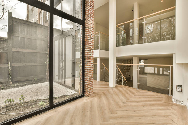 el interior de una casa con suelos de madera y puertas de vidrio que conducen a un área al aire libre que está bien mantenida - Foto, Imagen