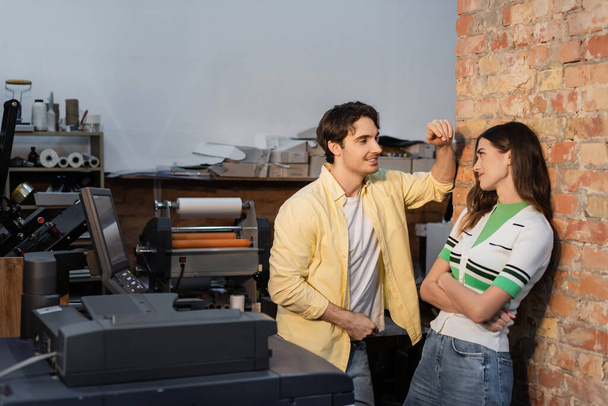 fröhlicher Mann flirtet mit hübscher Kollegin, während er zusammen im Druckzentrum steht  - Foto, Bild