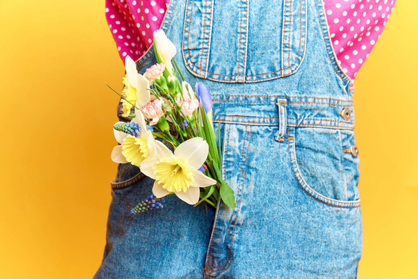 Fashion week. Cropped portrait with woman wearing vivid retro clothes and keeping flowers in pocket over yellow studio background. Concept of spring season, stylish clothes, beauty, art, creativity - Fotografie, Obrázek
