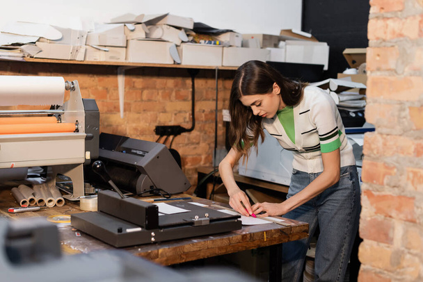 beschäftigter Typograph hält Messer in Papiernähe, während er im Druckzentrum arbeitet  - Foto, Bild