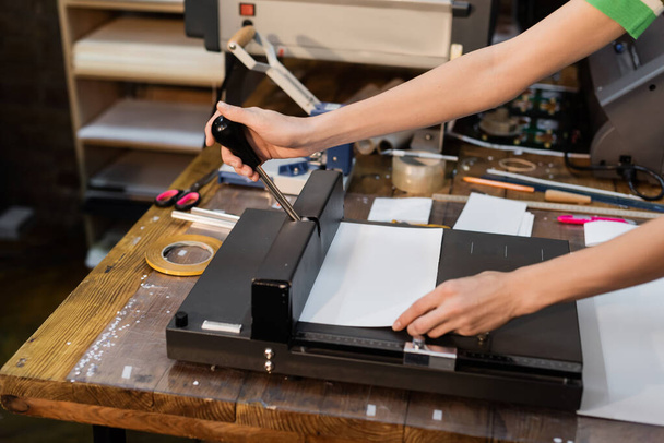 rajattu näkymä nainen leikkaamalla paperia, kun käytät trimmeri tulostuskeskus  - Valokuva, kuva