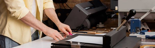 印刷センターバナー内のペーパートリマーの近くのナイフでタイポグラファー切断紙のクロップドビュー  - 写真・画像