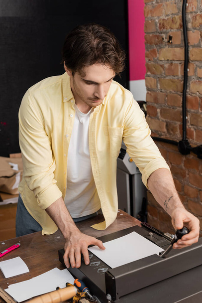 wytatuowany mężczyzna przy użyciu przycinarki do papieru w nowoczesnym centrum druku  - Zdjęcie, obraz