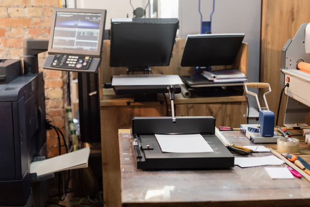 printcentrum met moderne apparatuur naast monitor en papieren trimmer  - Foto, afbeelding