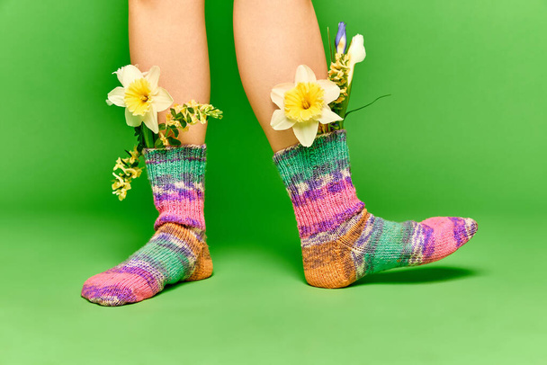 New spring trend. Creative portrait female feet with beautiful wildflowers inside colorful socks on green studio background. Closeup. Concept of spring season, stylish clothes, beauty, art, creativity - Photo, Image