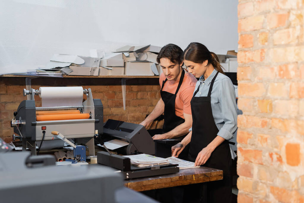 typographers in aprons looking at newspapers while working in print center  - Foto, imagen