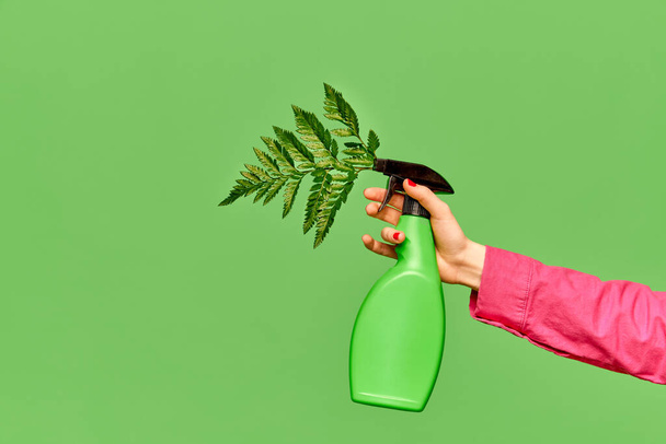 Весенний сад. Портрет с женской рукой, держащей поливающую бутылку с листьями растений на зеленом фоне студии. Природа, сезон цветения, стильная одежда, красота, искусство, креативность, реклама - Фото, изображение