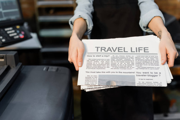 Teilansicht eines Typographen mit Tätowierung in der Hand, der frisch gedruckte Zeitungen hält  - Foto, Bild