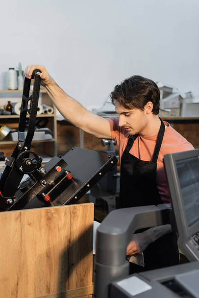 férfi kötényben professzionális nyomtatás plotter, miközben dolgozik a nyomtatási központ  - Fotó, kép