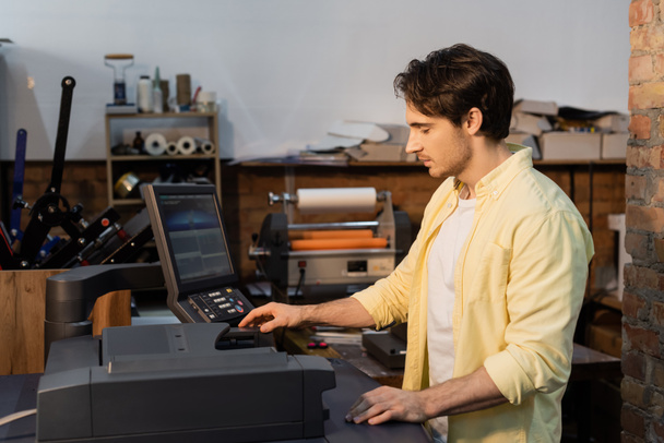 young man in yellow shirt using professional printer near monitor  - Foto, afbeelding