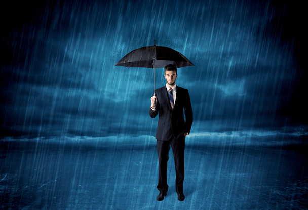 Business man standing in rain with an umbrella - Фото, зображення