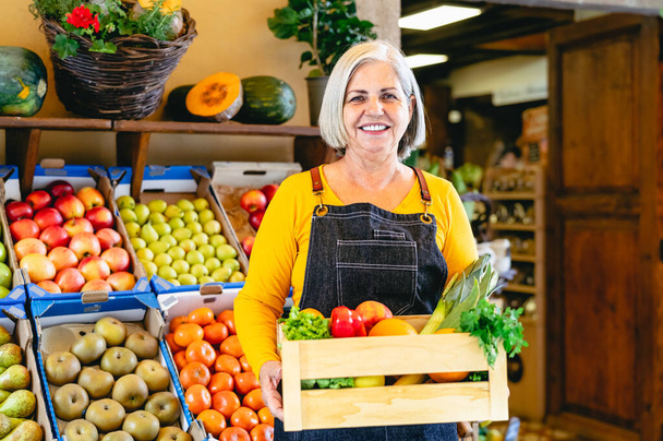 Female greengrocer working at the market holding a box containing fresh fruits and vegetables - Food retail concept - Photo, Image