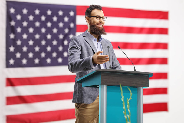 Bearded man giving a speech on a podium in front of an american flag - Фото, зображення