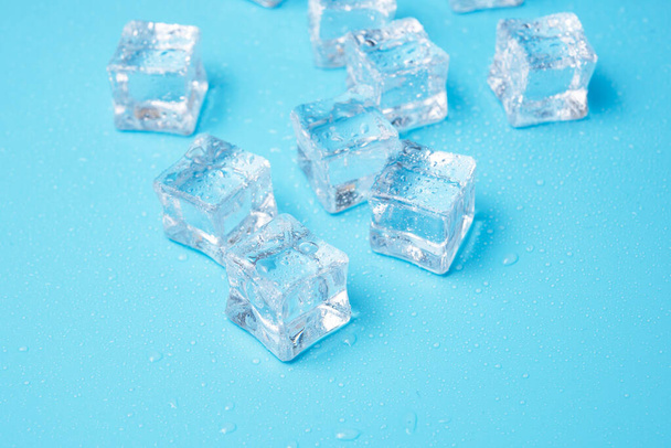 Кубики льоду з краплями води, розкиданими на синьому фоні, вид зверху
. - Фото, зображення