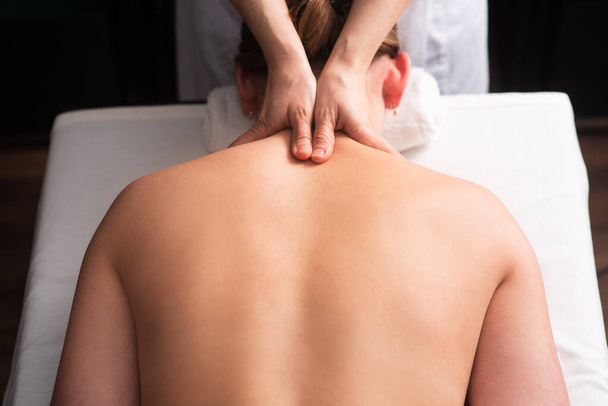 masér masíruje záda a lopatky mladé ženy na masážním stole na bílém pozadí. Koncept masážních lázeňských procedur. procedury uvolňování těla. Detailní záběr - Fotografie, Obrázek