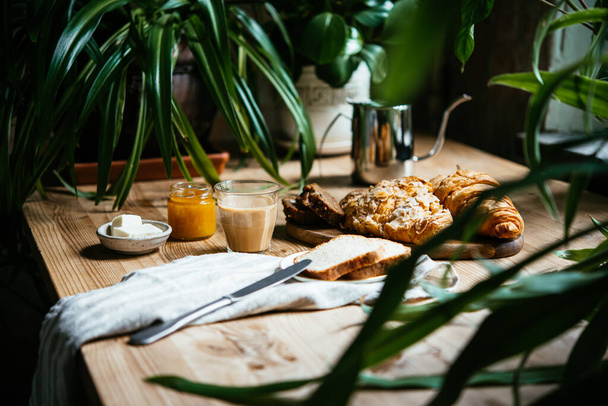 Breakfast with croissants and coffee served at a beautiful table full of plants. Enjoying time at home concept. - 写真・画像