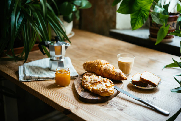 Breakfast with croissants and coffee served at a beautiful table full of plants. Enjoying time at home concept. - Valokuva, kuva