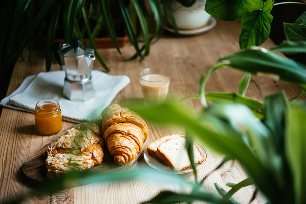 Breakfast with croissants and coffee served at a beautiful table full of plants. Enjoying time at home concept. - Foto, immagini
