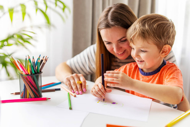 Η μητέρα και το παιδί ζωγραφίζουν με μολύβια στο γραφείο στο σπίτι. Ευτυχισμένη οικογένεια - Φωτογραφία, εικόνα