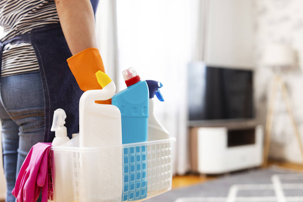 Kobieta w gumowych rękawiczkach z koszem środków czyszczących gotowa posprzątać mieszkanie. Gospodyni domowa ma wiele prac domowych, prac domowych i profesjonalnych usług sprzątania. Niska głębokość pola - Zdjęcie, obraz